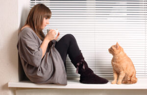orange cat staring at woman drinking coffee