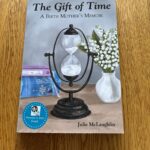 An hourglass next to a vase of flowers and a stack of 3 books.